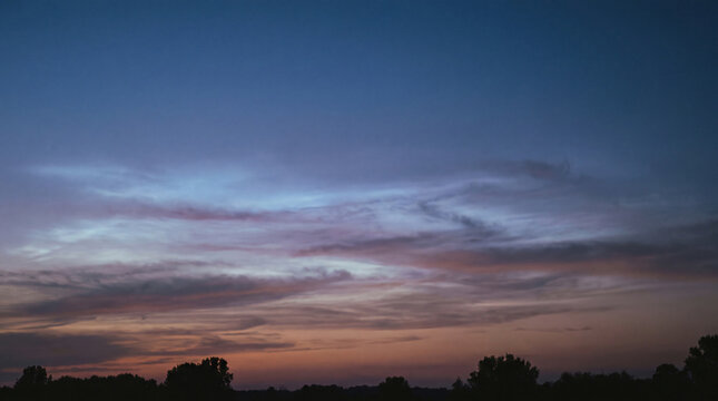 Dynamic twilight sky with streaks of colorful clouds, transitioning from deep blue to vibrant orange and purple over.