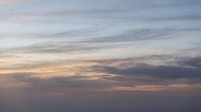 Atmospheric photograph of a serene evening sky with soft, wispy cirrus clouds and gentle pastel hues at dusk.