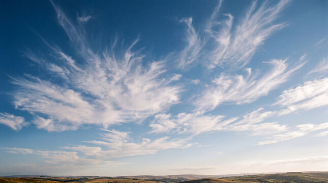 Expansive blue sky filled with gracefully sweeping cirrus clouds above a sunlit rolling landscape.