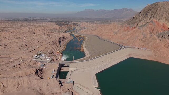 Stunning drone footage captures Dique Ullum dam, vibrant blue reservoir, arid desert terrain, rugged mountains, and winding river in San Juan, Argentina during summer.
