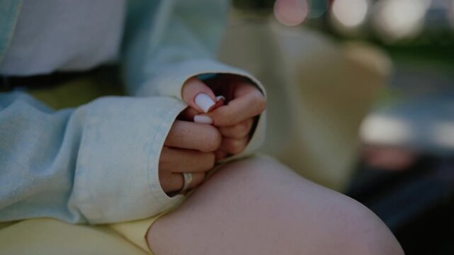 Close-up of stressed young woman hands nervously clasped on knee sitting on bench, fidgeting fingers revealing anxiety and impatience, waiting for important meeting, date, slow motion.