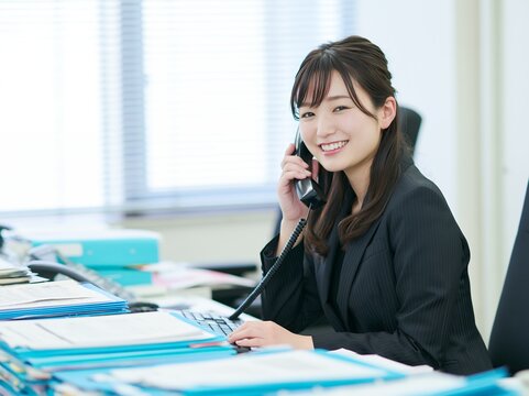 オフィスで電話応対する若く笑顔の日本人ビジネスウーマンの仕事風景