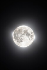 Obraz premium Full moon glowing brightly with a visible lunar surface set against a dark night sky background. Bright full moon with detailed craters and surface texture surrounded by a soft glowing white aura.