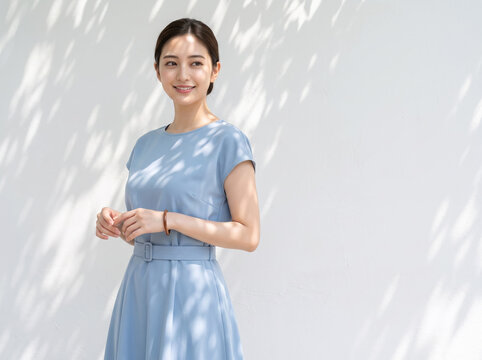 白い壁を背景に光と影の中で佇む水色のドレスの女性