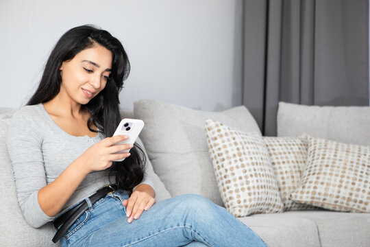 woman is using a phone sitting on a sofa