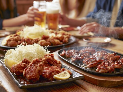 居酒屋で揚げ物と焼きたて肉料理を囲む人々がビールで乾杯