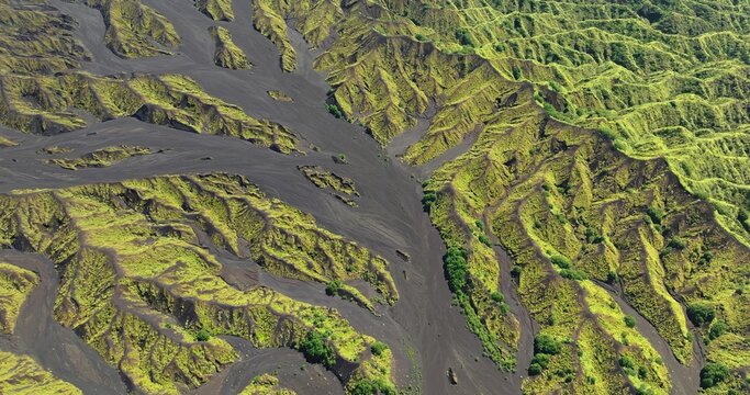 Aerial view of volcanic landscape featuring dark ash deposits contrasting with lush green vegetation on ridges in Port Resolution, Tanna Island, Vanuatu.