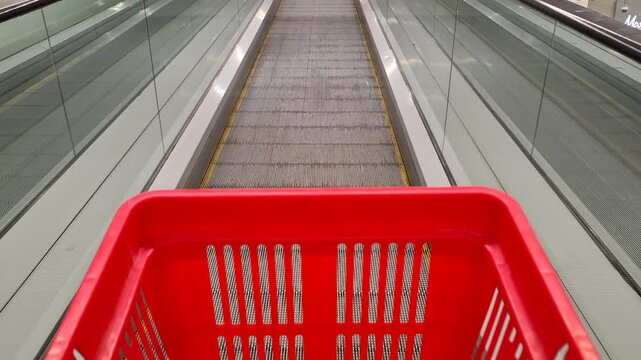 Red shopping basket moving along a store escalator, retail journey, consumer activity, and modern shopping lifestyle.