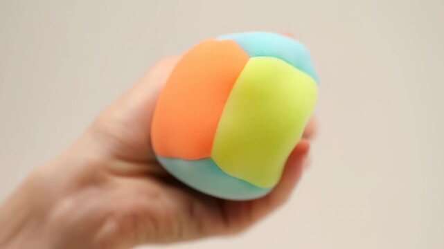 Hand squeezing multicolored squishy foam toy with rounded pastel sections on smooth beige background, soft light, shallow focus, playful tactile mood in clean minimalist scene