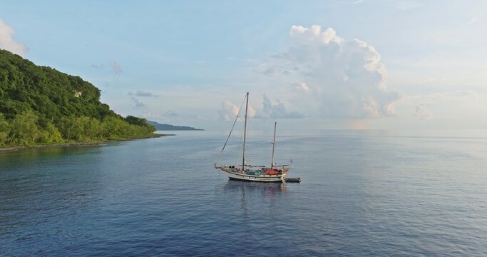 Aerial view of a sailboat anchored in the calm blue waters near the lush green coastline of Port Resolution, Tanna Island, Vanuatu.