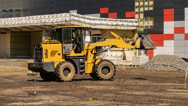 A construction vehicle is working on a site where workers are arranging materials. The area is full of dirt, with piles of gravel and other supplies present