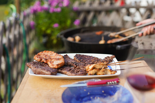 Man cooking meat on barbecue grill during summer evening party - Food, swiss culture and holiday concept - Focus on meat