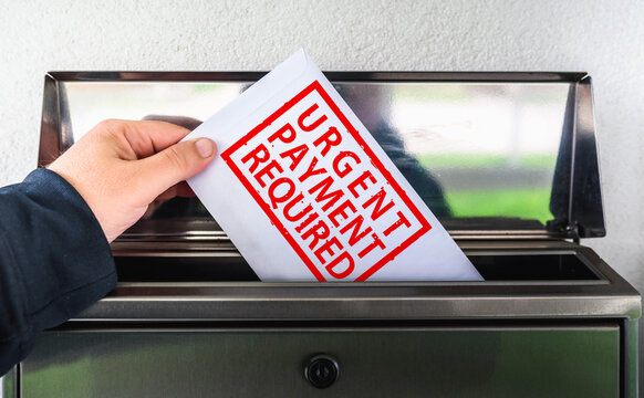 A hand holds an envelope with "URGENT PAYMENT REQUIRED" and is inserting it into a mailbox.