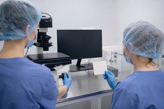 Lab technicians checking microscope equipment in sterile room