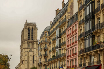 Obraz premium Notre Dame Cathedral tower rising above classic Haussmann buildings and a colorful pink facade in Paris, France