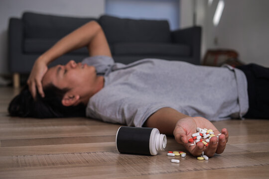Man Lying on Floor Holding Head in Pain with Pills Spilled in Hand and Bottle Nearby, Drug Overdose