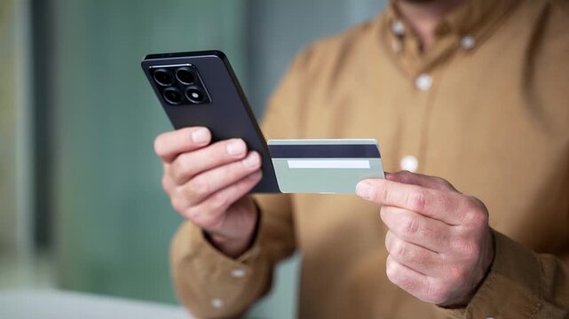 Close-up of businessman hands entering credit card details on a smartphone while sitting at a desk in a modern business office. Secure online payment and digital banking transaction concept.