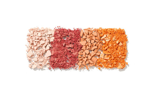 Row of four crumbled eyeshadow swatches in beige, deep red, brown beige, and orange isolated on white background. Broken cosmetic powder texture, colored pigments for beauty and makeup design.
