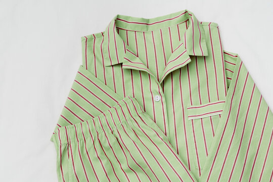 Soft green Pajamas folded on white sheet background. Top view stylish sleepwear of natural fabric. Cozy striped pyjamas for sleeping, loungewear fashion details, concept of rest, healthy sleep.
