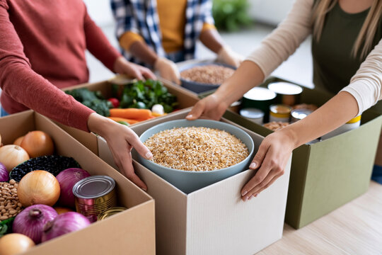 Group of diverse individuals organizing food items into boxes, including grains, vegetables, and canned goods, in a bright indoor setting with natural light