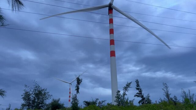 Low angle tilt up shot of wind turbines spinning under dramatic twilight sky with power lines in Quy Nhon Vietnam