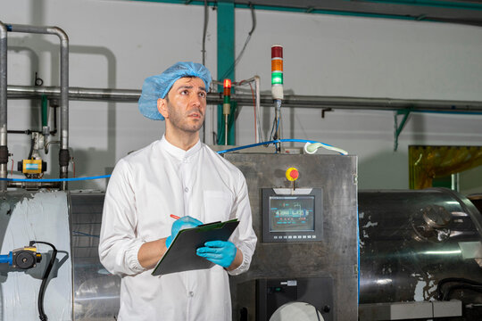 Confident mature male worker in white uniform and blue rubber gloves working in food factory.