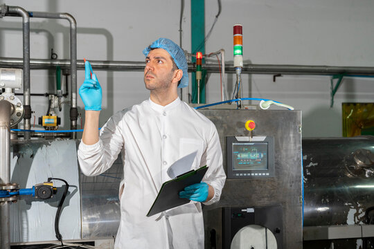 Confident mature male worker in white uniform and blue rubber gloves working in food factory.