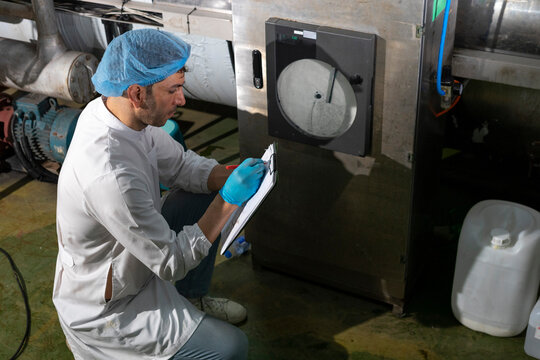 Confident mature male worker in white uniform and blue rubber gloves working in food factory.