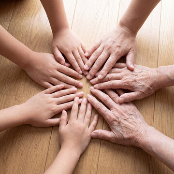 Overhead view of diverse hands joined in circle palms down on clean wood floor in soft natural light