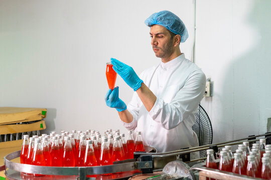 Portrait of mature male researcher with bottle of red beverage in bottle factory.