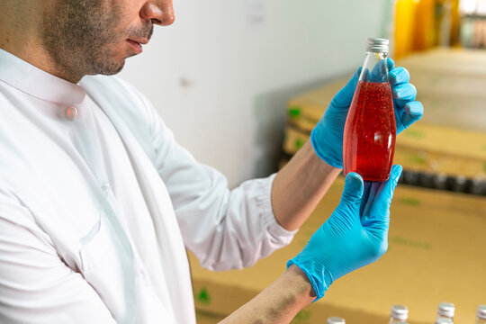 Portrait of mature male researcher with bottle of red beverage in bottle factory.