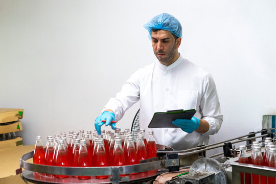Portrait of mature male researcher with bottle of red beverage in bottle factory.