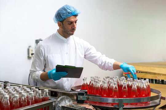 Portrait of mature male researcher with bottle of red beverage in bottle factory.