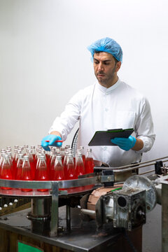 Portrait of mature male researcher with bottle of red beverage in bottle factory.