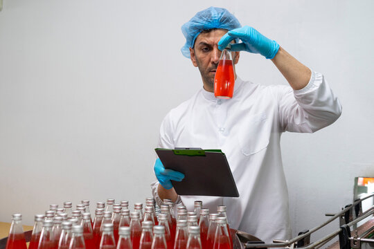 Portrait of mature male researcher with bottle of red beverage in bottle factory.