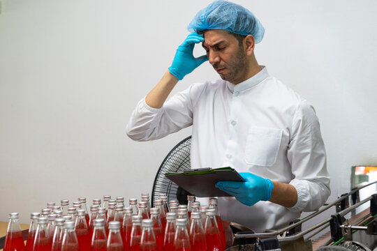Mid adult industrial worker feeling tired and exhausted at bottle conveyer belt in factory. 