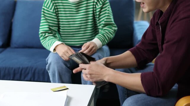 Young couple arguing about financial problems, showing empty wallet and unpaid bills on the table.