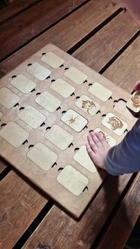 Child's hands interacting with wooden memory game featuring laser-cut tiles with animal engravings on rustic wooden table, educational toy playtime, tactile learning experience.