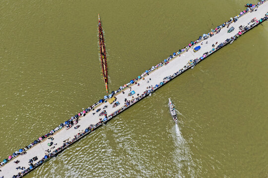 Aerial view of a traditional long boat race with rowers in the river near a crowded bridge filled with spectators in Sirajganj, Rajshahi Division, Bangladesh.