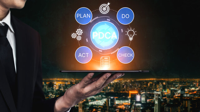 Businessman Holding Tablet with PDCA Cycle Concept Over Cityscape Background for Effective Management and Continuous Improvement Strategies. Bitwise.