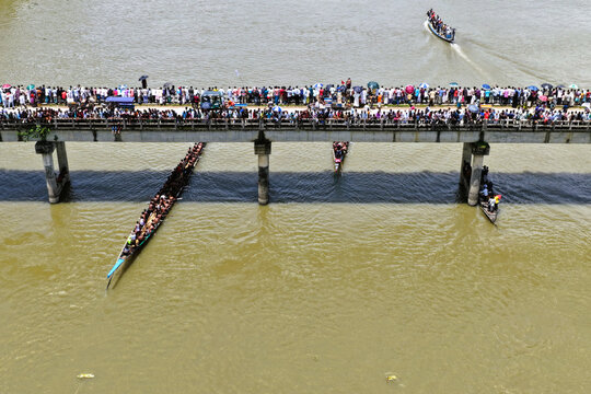 Aerial view of a traditional boat race on the river with long boats filled with rowers and a large crowd of spectators gathered on the bridge in Sirajganj, Rajshahi Division, Bangladesh.