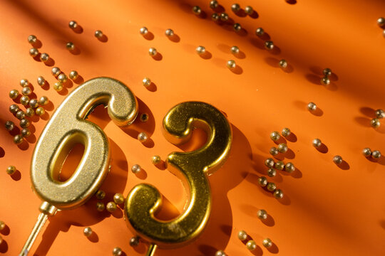 vibrant festive backdrop for 63rd birthday, made of gold candles shaped like number sixty-three, placed on an orange background with sprinkles. versatile festive banner