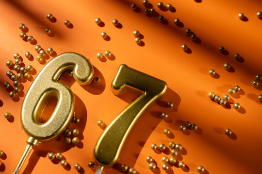vibrant festive backdrop for 67th birthday, made of gold candles shaped like number sixty-seven, placed on an orange background with sprinkles. versatile festive banner