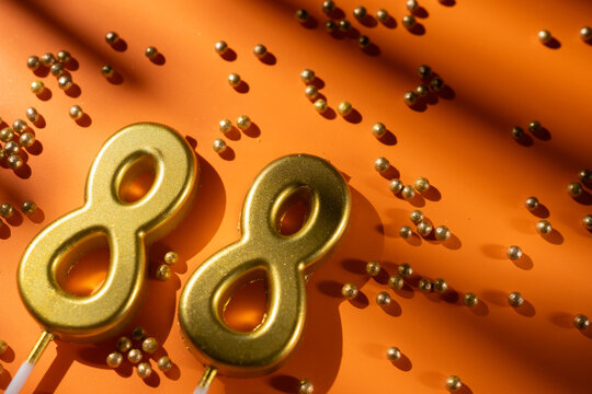 vibrant festive backdrop for 88th birthday, made of gold candles shaped like number eighty-eight, placed on an orange background with sprinkles. versatile festive banner