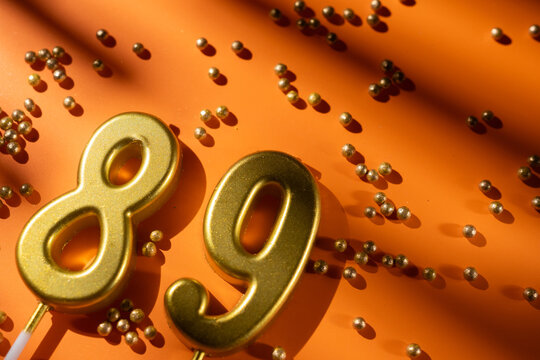 vibrant festive backdrop for 89th birthday, made of gold candles shaped like number eighty-nine, placed on an orange background with sprinkles. versatile festive banner