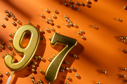 vibrant festive backdrop for 97th birthday, made of gold candles shaped like number ninety-seven, placed on an orange background with sprinkles. versatile festive banner