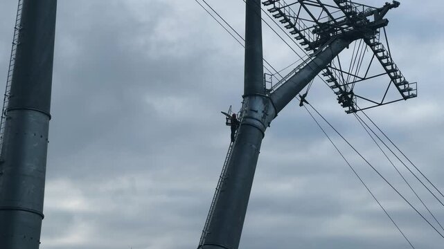 Industrial worker climbing large high altitude electrical tower (power transmission support). Electrician-lineman installation voltage overhead lines climber. Metal pipe maintenance, engineering labor