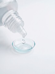 Fototapeta premium Contact lens care solution dripping into clear contact lens on white background, vision care and optical hygiene concept