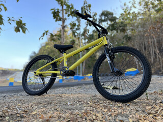 Fototapeta premium Yellow BMX bicycle photographed beside a countryside road near a tropical teak forest from a low front angle under sunny skies.