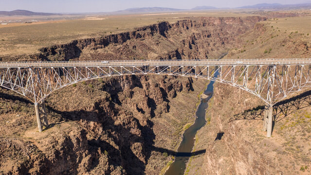 Aerial view of the Rio Grande Gorge Bridge spanning the deep volcanic canyon with the Rio Grande river flowing below in Taos County, New Mexico, United States.